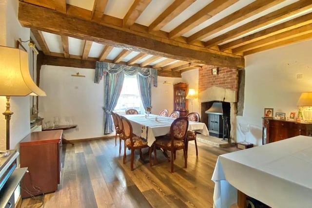 The dining room includes a feature stone and brick fireplace with stove. The ceiling is heavily beamed, and there are inset timber frames to the walls.