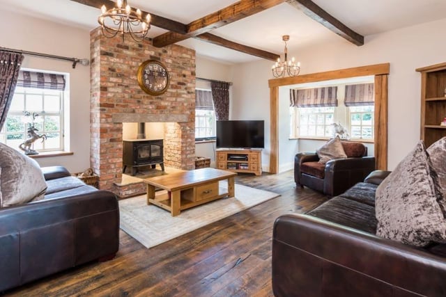 The grand living room features an impressive brick fireplace at its centre, with wooden beams on the ceiling, hard wood floors, and enough seating to accommodate family and guests.
