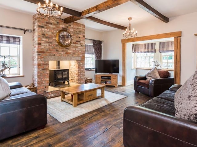 The grand living room features an impressive brick fireplace at its centre, with wooden beams on the ceiling, hard wood floors, and enough seating to accommodate family and guests.
