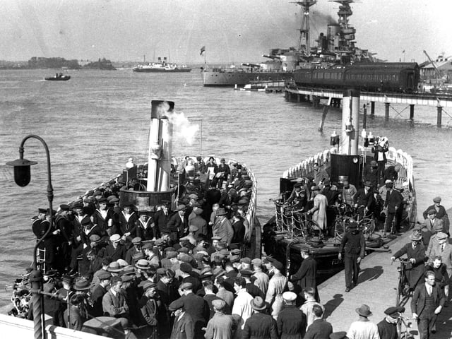 A packed Gosport Ferry in 1936.
We see Dockyard men, sailors and ordinary folk boarding and alighting two Gosport Ferries.
To the rear can be seen the railway viaduct that linked the harbour Station to the South Railway Jetty.
Tied up at the jetty is a pre-war battleship and to the left of her are two Isle of Wight paddle steamers. Image courtesy of Sid Greeman.