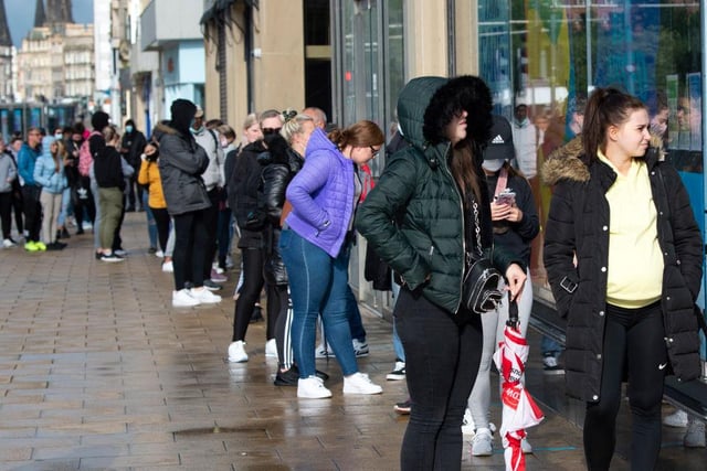 Shoppers wait to enter stores in the rain