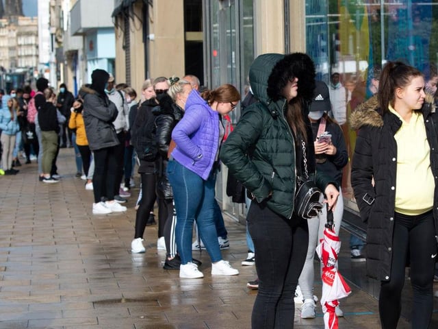 Shoppers wait to enter stores in the rain