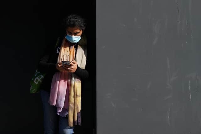 A woman wearing a face mask checks her phone (Photo by Ian Forsyth/Getty Images)