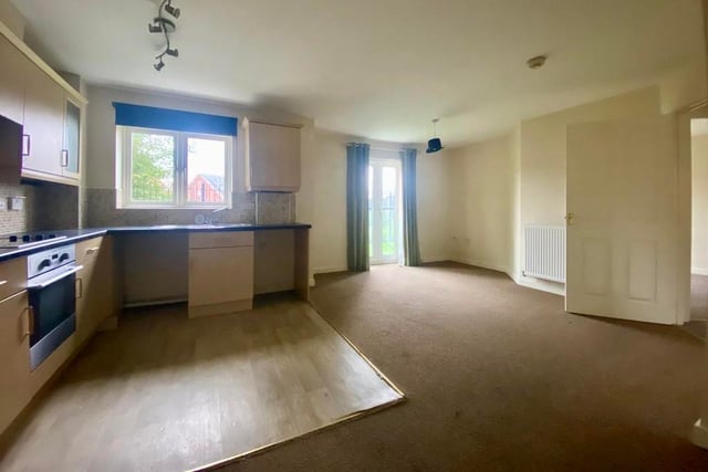 This photo shows how the kitchen (left) opens out to the lounge. It is a pleasant space, with patio doors, carpeted flooring and a double radiator.
