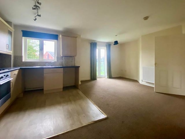 This photo shows how the kitchen (left) opens out to the lounge. It is a pleasant space, with patio doors, carpeted flooring and a double radiator.