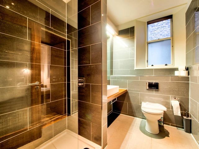 The bathroom comes fully-equipped with a standing shower and bath, as well as a toilet and a sink, with modern tiling and a window for ventilation.