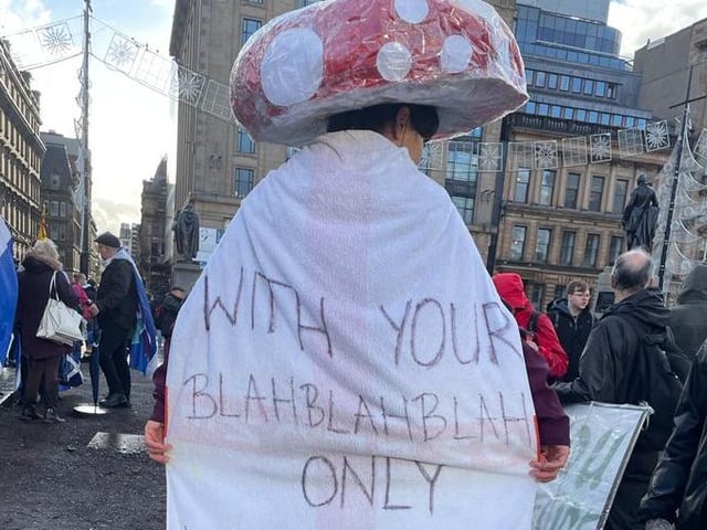 An activist with a mushroom top on their head and a sign which reads: "With your blah blah blah only mushrooms will survive."
