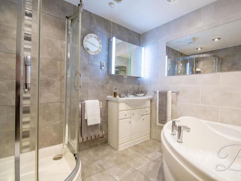 The enchanting en suite to the main bedroom. It includes a fully-tiled suite, fitted with a corner bath, vanity unit, chrome radiator, enclosed shower and a low-flush WC.