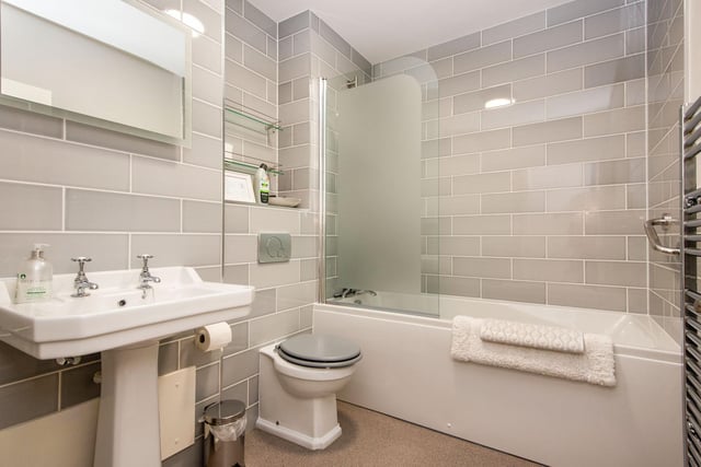 The bathroom was put in only recently and includes a bath with shower, a chrome heated towel rail, and ceramic grey brick tiles.