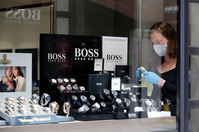 A retail worker wearing PPE (personal protective equipment), of gloves, a face mask or covering as a precautionary measure against COVID-19, arranges a display of watches in a jewellery store, recently re-opened at Gunwharf Quays.