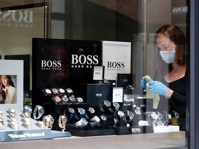 A retail worker wearing PPE (personal protective equipment), of gloves, a face mask or covering as a precautionary measure against COVID-19, arranges a display of watches in a jewellery store, recently re-opened at Gunwharf Quays.