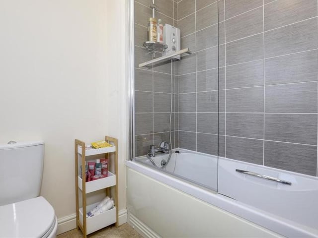 The second look at the family bathroom reveals a panelled bath with a wall-mounted electric shower. The walls are partially tiled and there is also an extractor fan with a uPVC double-glazed, opaque window to the back of the house.