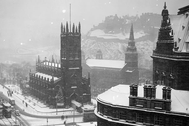 Edinburgh Castle as snow falls on the West End of Princes Street with St John's Church and St Cuthbert's church in the foreground (and a Christmas tree to left of the entrance) and the frontage of the Caledonian Hotel to the right. December 1950