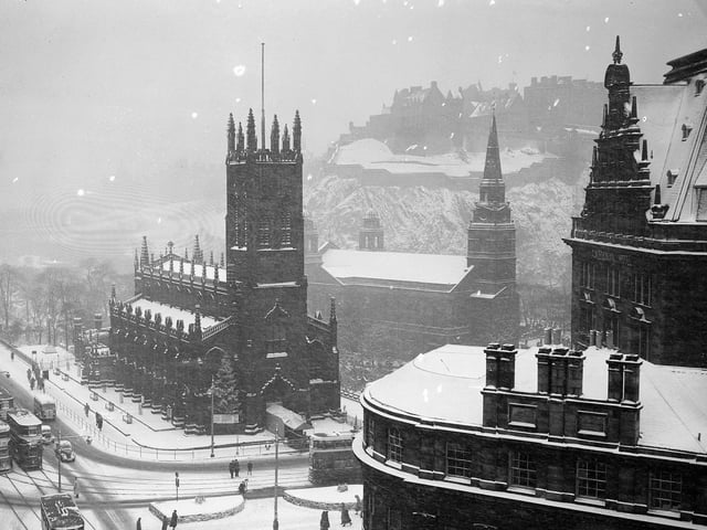 Edinburgh Castle as snow falls on the West End of Princes Street with St John's Church and St Cuthbert's church in the foreground (and a Christmas tree to left of the entrance) and the frontage of the Caledonian Hotel to the right. December 1950