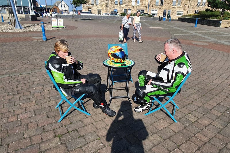 Two cool-looking bikers enjoy a nice coffee by the town square. Cool suits too!
