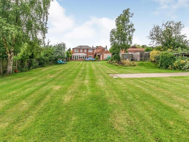 The back garden, which is mainly laid to lawn. It also has patio areas, lighting, a tap, a pond and small sheds.