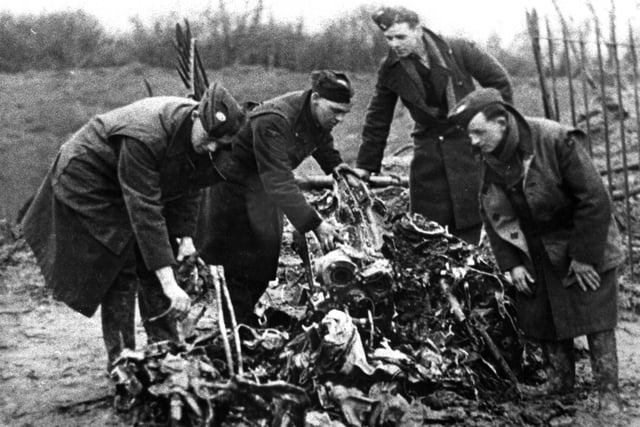 Servicemen hunt through the crumpled remains of the Heinkel which crashed and exploded in Beach Road in February 1941.