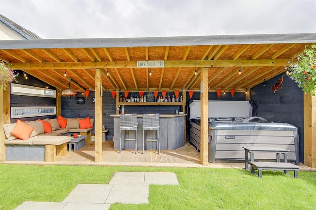 An outdoor entertaining area, complete with seats, a bar, and hot tub.