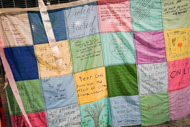 Quilted sheets displaying environmental and climate messages are hung on the outside of perimeter fence of the SEC