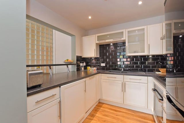 The kitchen contains cream-coloured units and contrasting worktops, an integrated dishwasher, a breakfast bar and a feature 'glass block' wall.
