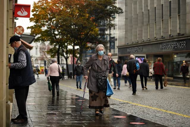 A woman wearing a face mask walks along the pavement in the shopping district in central Sheffield (Photo by OLI SCARFF/AFP via Getty Images)