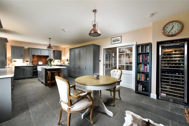 The open plan dining kitchen has hand made painted units, flagstone flooring, marble worktops, a central island, gas range cooker, and warming wood burning stove.