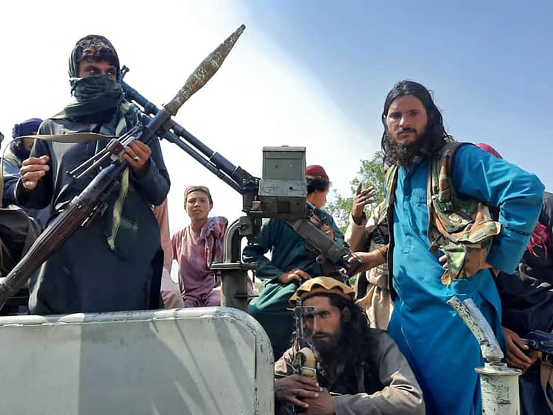 Taliban fighters sit over a vehicle on a street in Laghman province