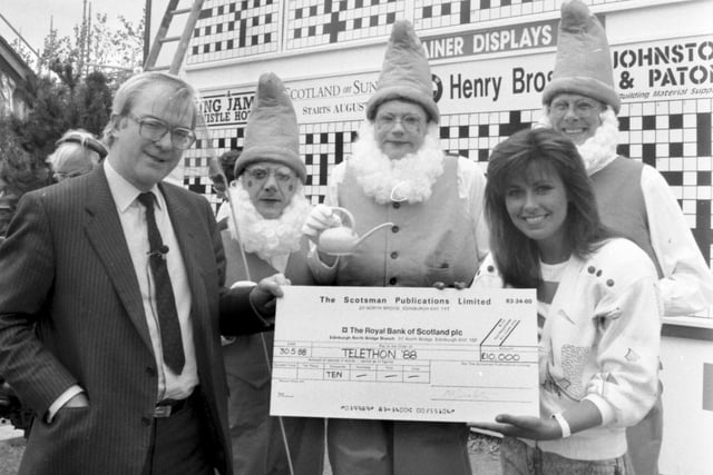 The then Scotsman newspaper editor Magnus Linklater presents Debbie Greenwood with a cheque for Telethon 88 at Glasgow Garden Festival in May 1988. Three men dressed as garden gnomes look on.