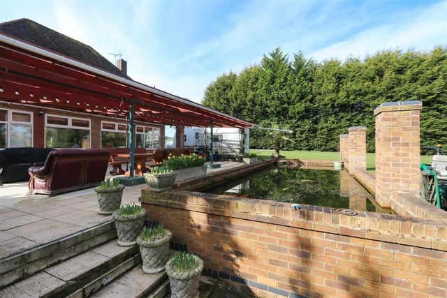 The large, covered patio  looks out onto a pond and a garden beyond the water feature.