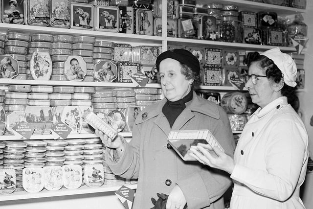 Two shoppers selecting from a range of tins of toffees in in 1958.