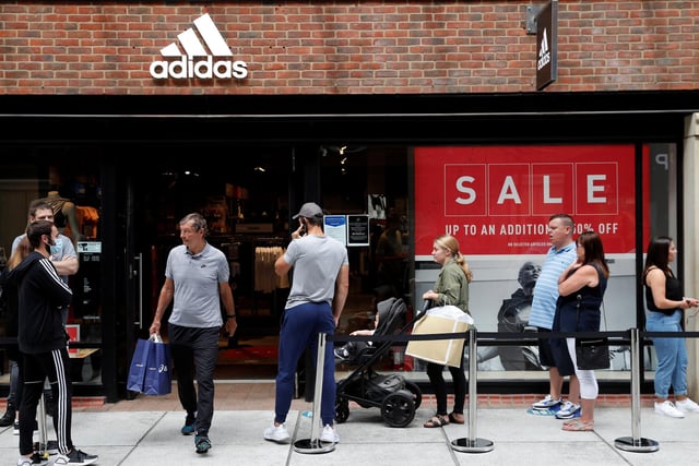 Shoppers, some wearing PPE (personal protective equipment), of a face mask or covering as a precautionary measure against COVID-19, queue to enter a recently re-opened Adidas store at Gunwharf Quays