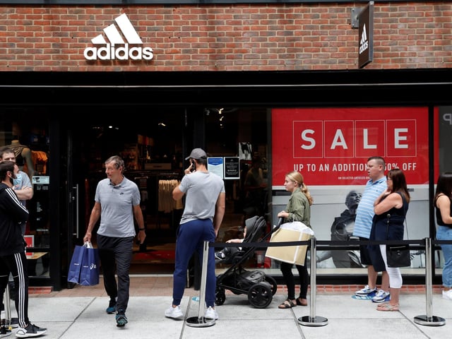 Shoppers, some wearing PPE (personal protective equipment), of a face mask or covering as a precautionary measure against COVID-19, queue to enter a recently re-opened Adidas store at Gunwharf Quays