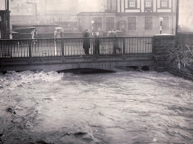 People look anxiously from Heeley Bridge during the Sheffield floods on July 2, 1958, as the little Sheaf rises dangerously close to street level.