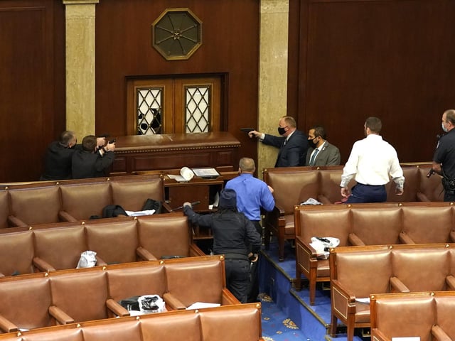 U.S. Capitol police officers point their guns at a door that was vandalized in the House Chamber during a joint session of Congress