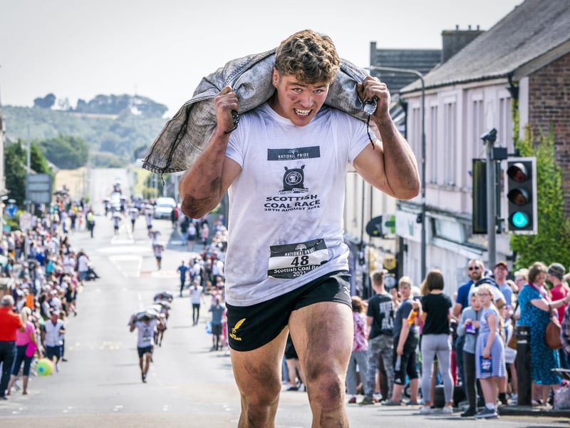 Wallace Nelson, from Kinross, goes on to win the Mens Race in the Scottish Coal Carrying Championships through the streets of Kelty in Fife. Picture date: Saturday August 28, 2021. PA Photo. The annual event is one of only two Coal Races in the world and the men's race requires participants to carry a 50-kilo bag of coal and the women's race requires a 25-kilo bag of coal to be carried over 1000 metres through the village. Photo credit should read: Jane Barlow/PA Wire