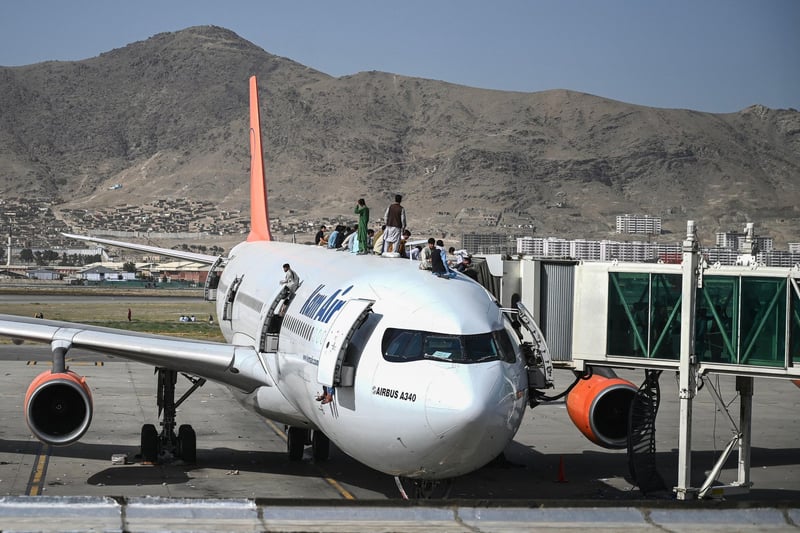 Afghan people climb atop a plane as they wait at the Kabul airport in Kabul after a stunningly swift end to Afghanistan's 20-year war, as thousands of people mobbed the city's airport trying to flee the group's feared hardline brand of Islamist rule.