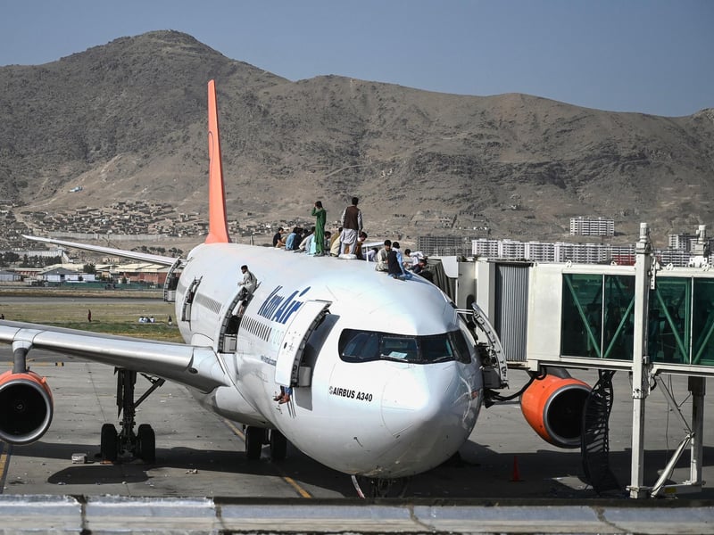Afghan people climb atop a plane as they wait at the Kabul airport in Kabul after a stunningly swift end to Afghanistan's 20-year war, as thousands of people mobbed the city's airport trying to flee the group's feared hardline brand of Islamist rule.