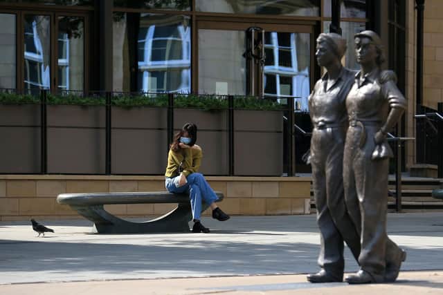 A woman wearing PPE (personal protective equipment), including a face mask as a precautionary measure against COVID-19, sits on a bench in Sheffield (Photo by LINDSEY PARNABY/AFP via Getty Images)
