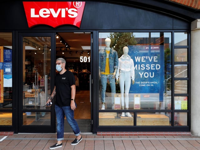 A retail worker wearing PPE directs customers waiting to enter a Levi's clothes store at Gunwharf Quays.