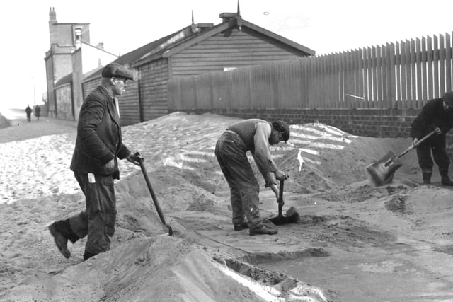 Workmen take advantage of a calm day to clear away sand whipped wall high at the entrance to Shields Pier in 1962.