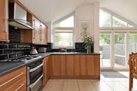 The kitchen has wood effect wall and base units with contrasting black laminate worktops and black brick shaped tiled splash back. Integrated appliances include gas hob, electric oven, extractor and dishwasher.