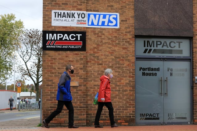 Shoppers walk past a banner saying thank you to the NHS on the first day of tough new coronavirus rules in Sutton