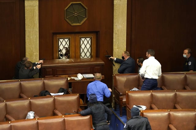 Law enforcement officers point their guns at a door that was vandalised in the House Chamber during a joint session of Congress