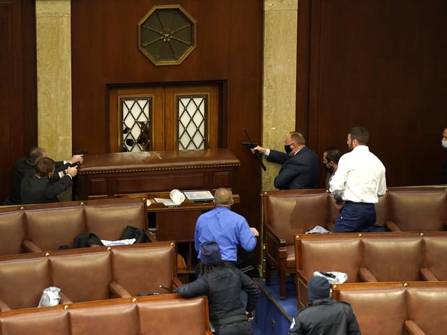 Law enforcement officers point their guns at a door that was vandalised in the House Chamber during a joint session of Congress