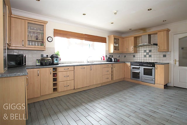 The kitchen features a double bowl stainless steel sink, a large double glazed window overlooking the front garden and wood effect tiling to the floor.