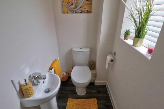 A downstairs toilet comprises a two-piece white suite with tiling to the wet areas, a wood-effect, cushioned floor and an opaque uPVC double-glazed window.