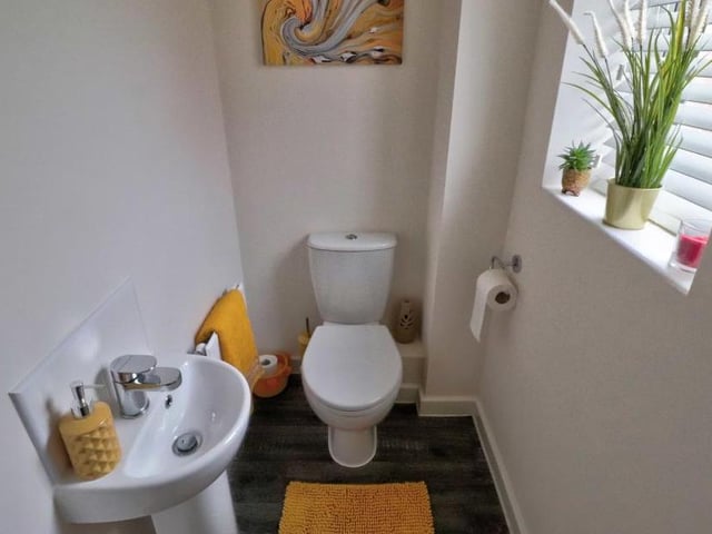 A downstairs toilet comprises a two-piece white suite with tiling to the wet areas, a wood-effect, cushioned floor and an opaque uPVC double-glazed window.