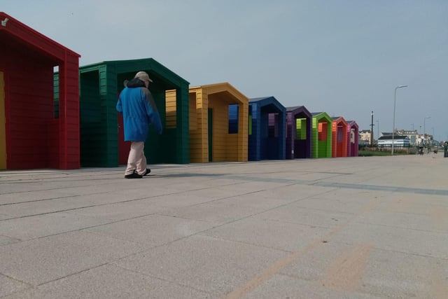 A resident takes his daily walk by the colourful beach huts.