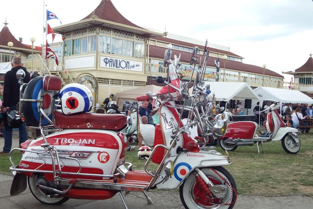 The local International Scooter festival in Ryde on the IOW back on 2014. Scooters parked outside the Pavilion, 3 Mods admire a scooter and have a drink and a chat.