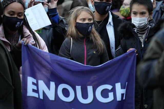 Climate change activist Greta Thunberg stoically stands in front of a banner reading 'Enough is Enough'